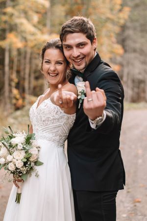 Newlyweds showing off their rings in a playful autumn forest portrait.
