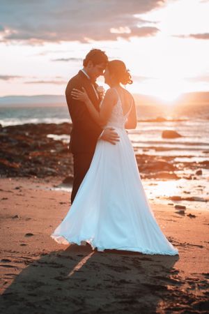Romantic silhouetted couple sharing a tender moment at sunset on a beach with crashing waves in the background.