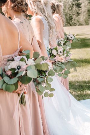Row of bridesmaids in blush pink dresses holding elegant bouquets with eucalyptus and roses.
