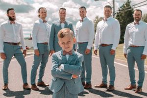 Wedding party in light blue suits posing playfully with a young boy in matching attire standing in front.