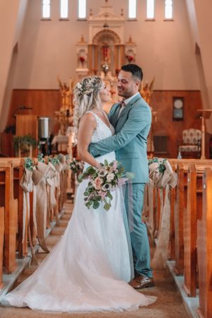 Romantic wedding moment captured in a traditional church with wooden pews and decorated aisle.
