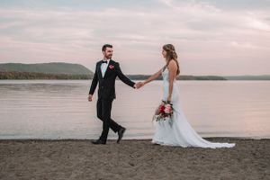 Newlyweds walking on beach at sunset holding hands.
