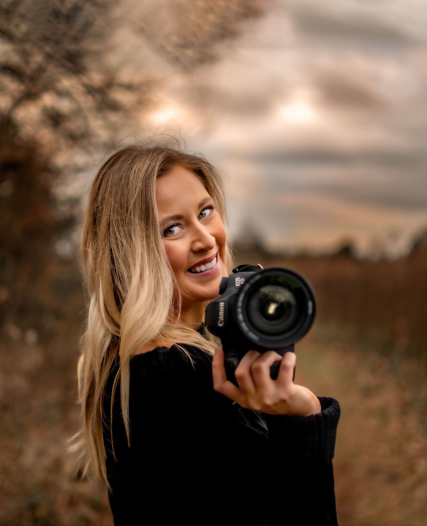 Photographer with professional camera smiling in warm sunset lighting.