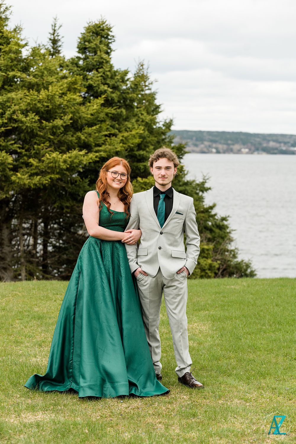 Formal couple poses by waterfront, emerald dress and light gray suit.