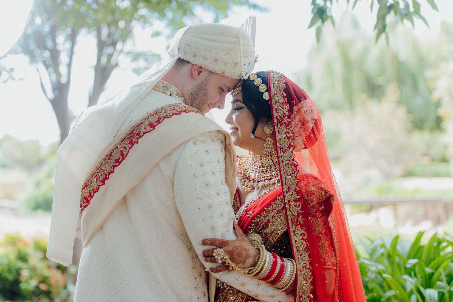 Wedding couple in traditional Indian attire sharing an intimate moment outdoors.