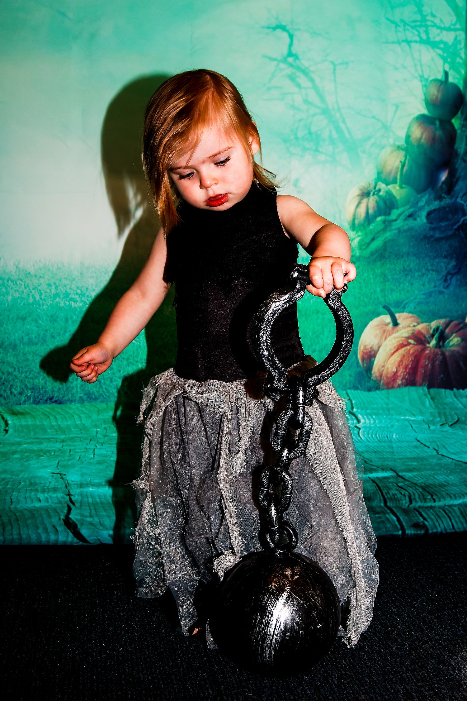 Dramatic photo of child with chain prop against ethereal green Halloween backdrop.