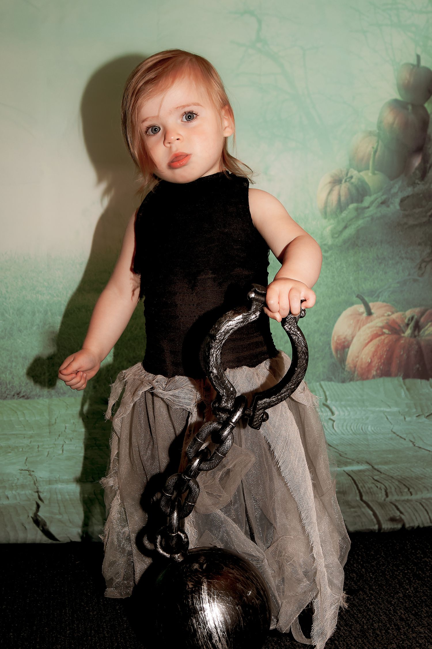 Child in dark costume holds chain and ball prop against mystical background.