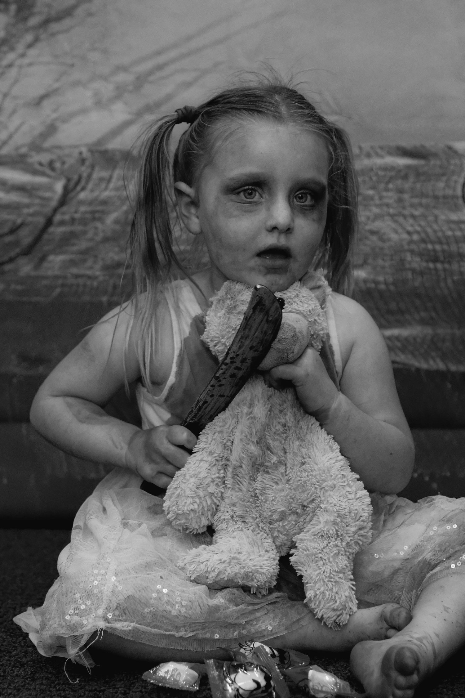 Black and white Halloween portrait with child holding stuffed toy in eerie setting.