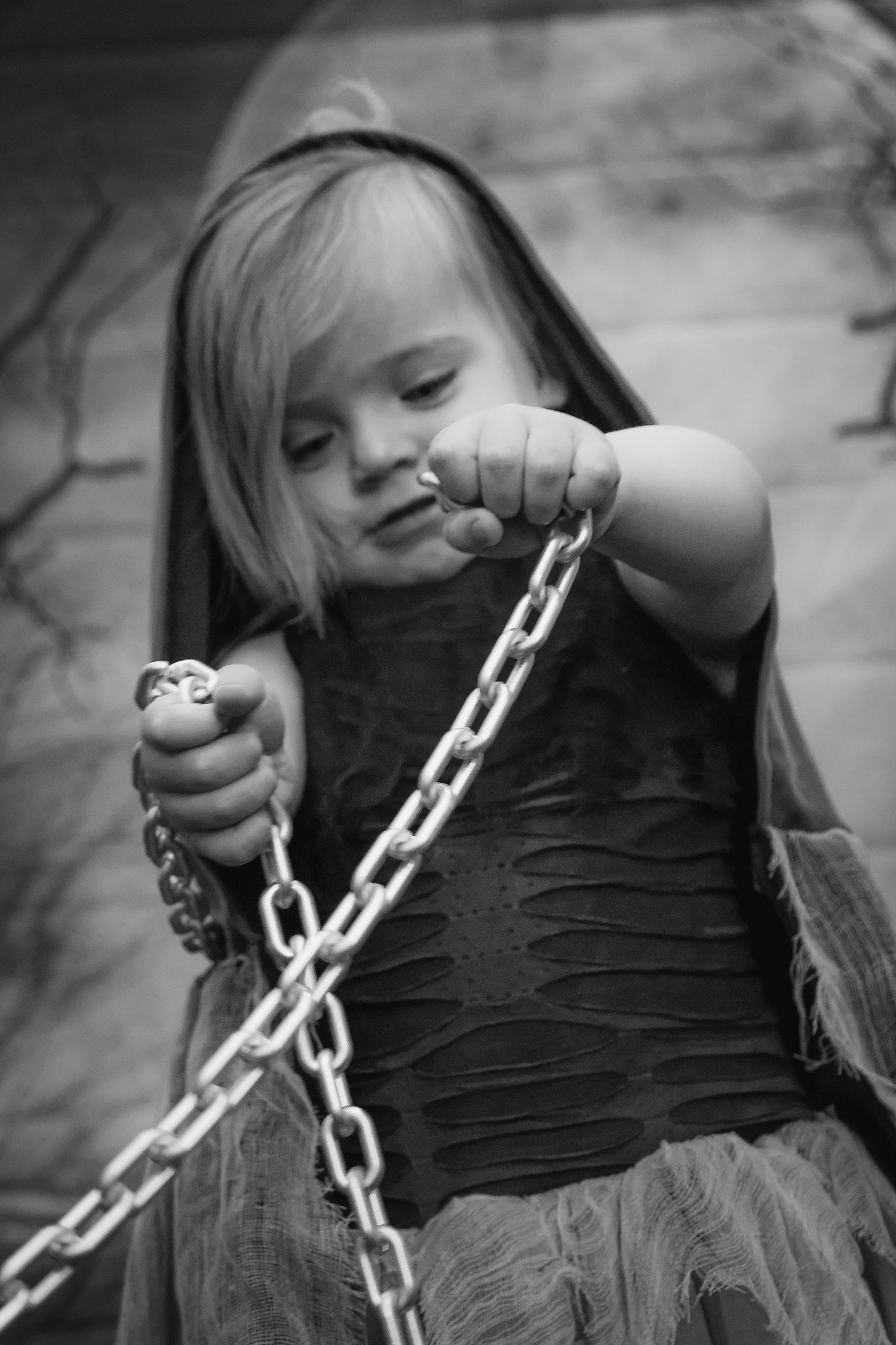 Black and white portrait of young child in dark dress holding metal chains outdoors.