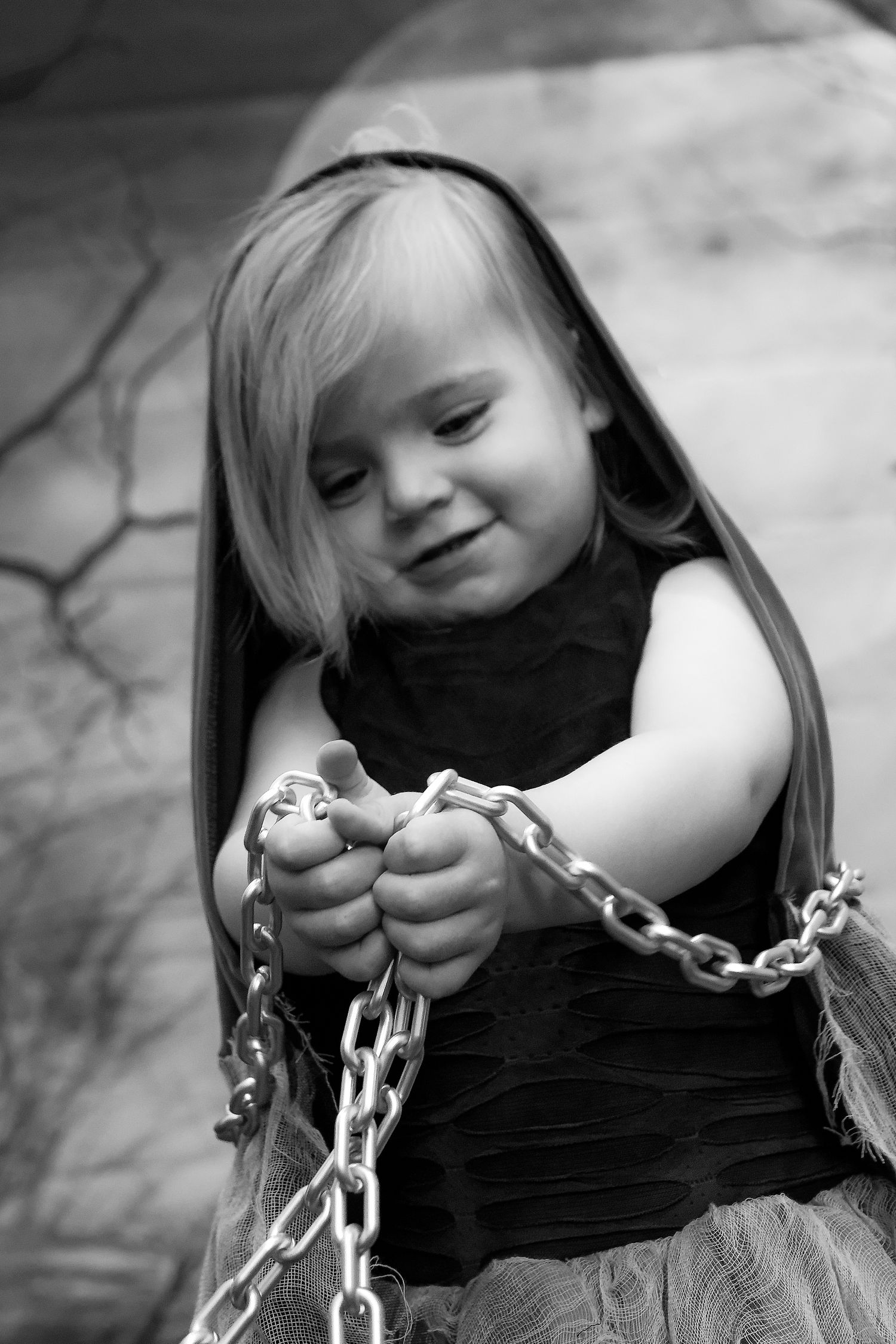 Black and white closeup of small child smiling while holding chain links.