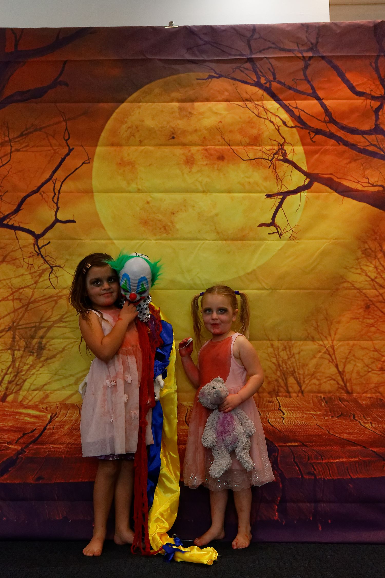 Children holding props against spooky orange backdrop with silhouetted tree branches.