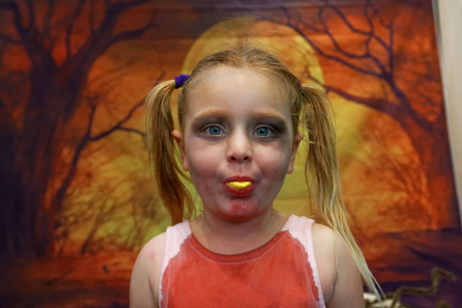 Young performer in orange tank top against spooky orange backdrop with trees.
