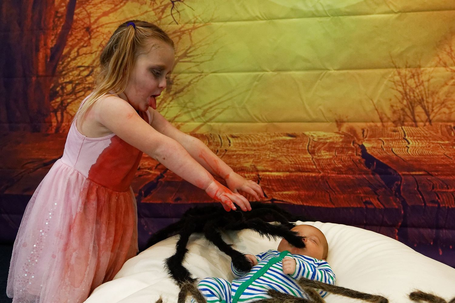 Child reaching towards puppet props on white bean bag against sunset backdrop.