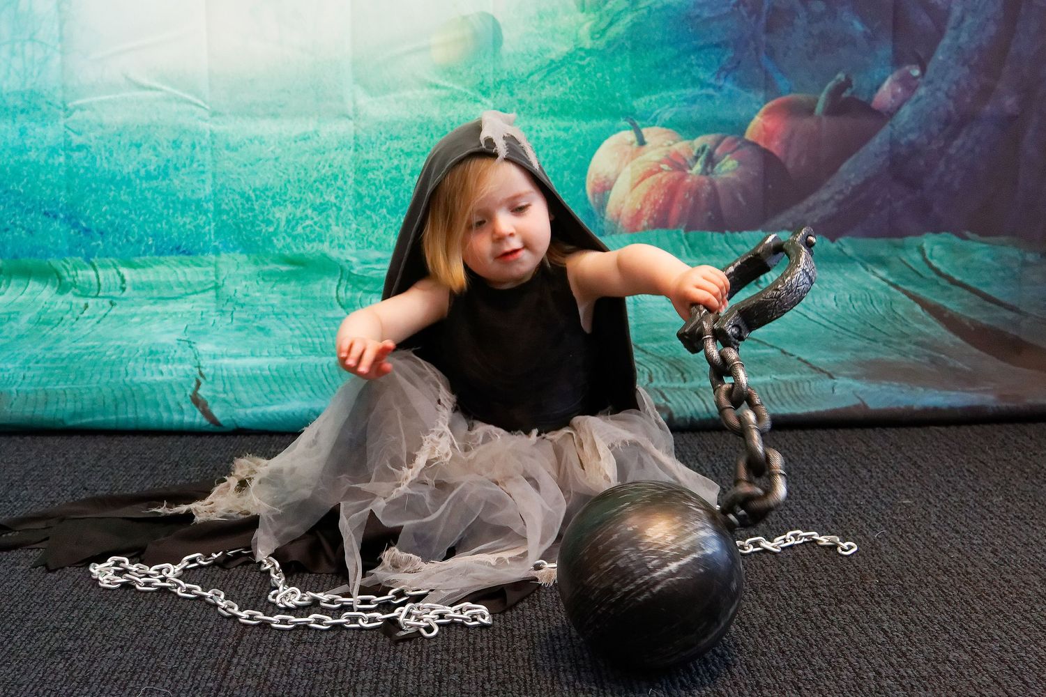 Child in black dress and gray tulle skirt posing with prop ball and chain on floor.