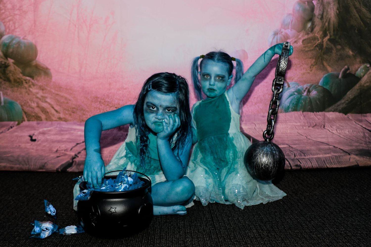 Creepy Halloween portrait with blue lighting shows two figures posing with a cauldron and chain.