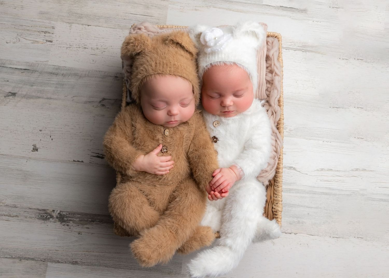 Two sleeping babies in teddy bear and lamb costumes lying together on a rustic wooden floor.
