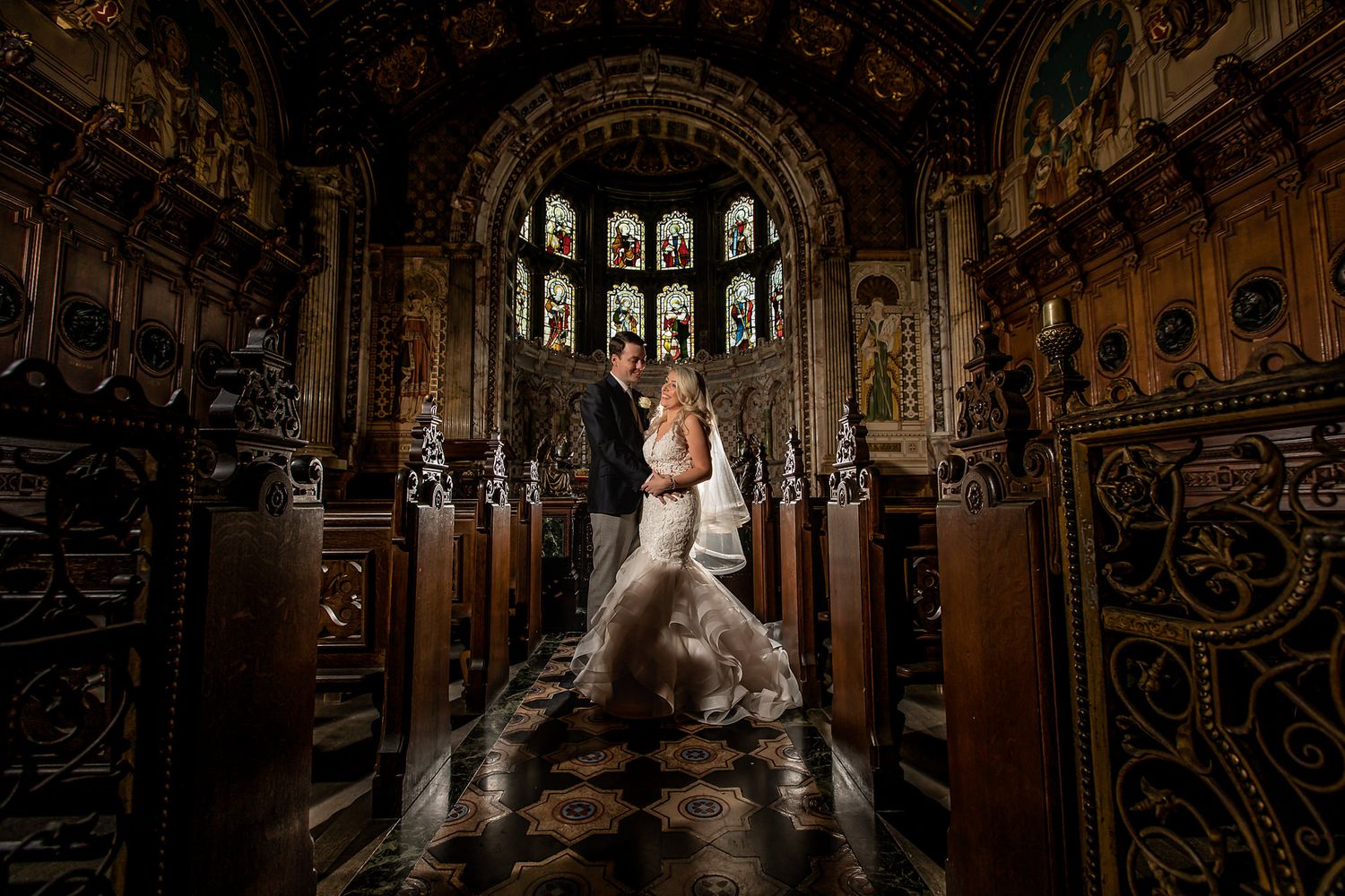 Stunning gothic chapel interior with ornate woodwork frames a wedding portrait.