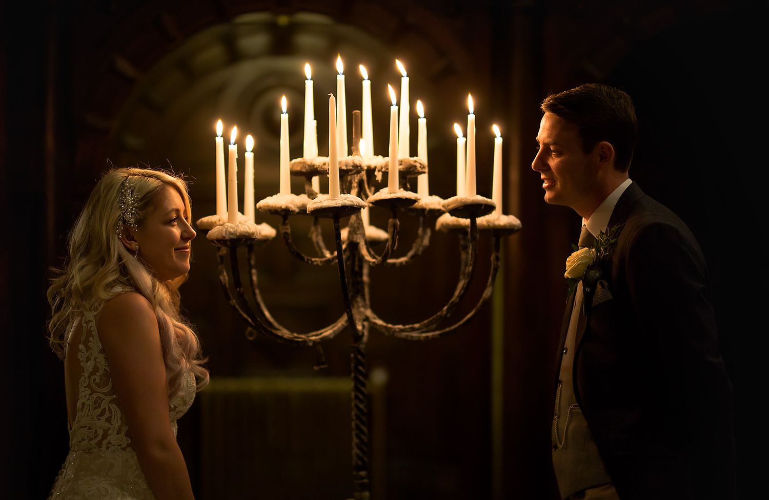 A romantic wedding moment illuminated by glowing candelabra in a darkened room.