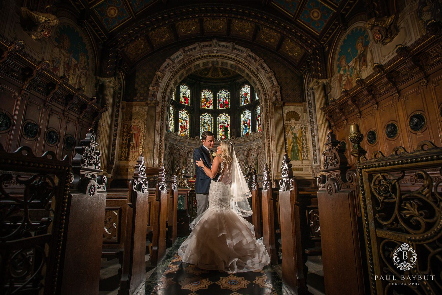 Dramatic wedding photo in historic chapel with stained glass windows and ornate architecture.
