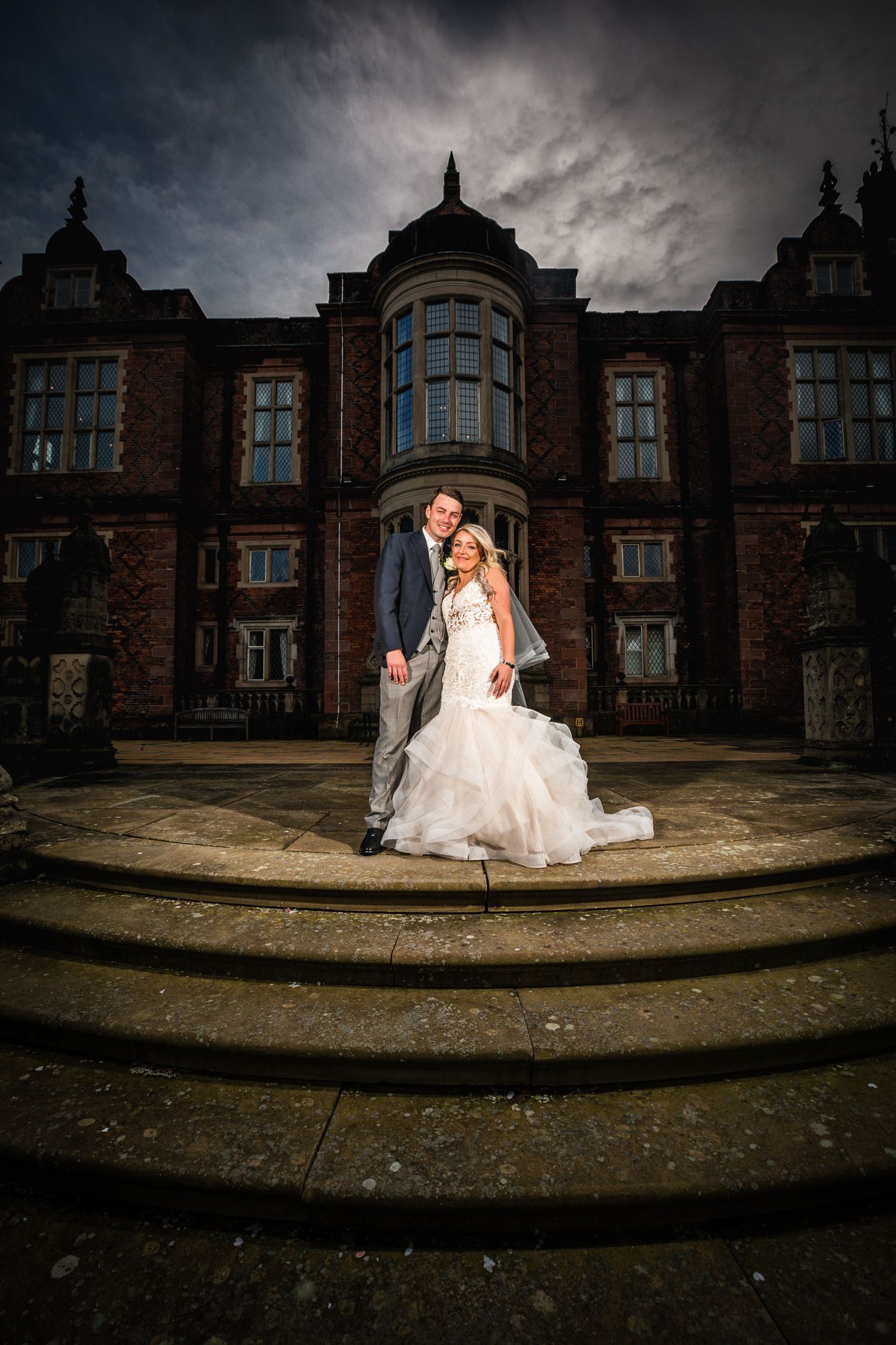 Dramatic wedding portrait in front of a grand Victorian mansion with stormy skies.