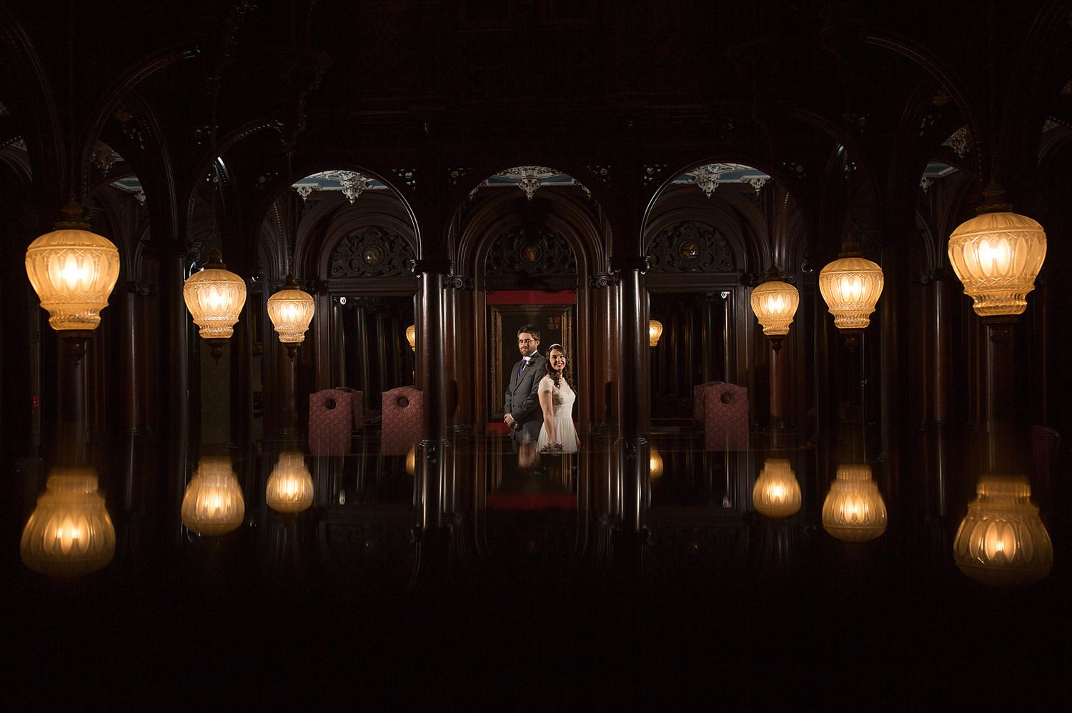 Dramatic wedding photo with glowing pendant lights in dark gothic hallway.