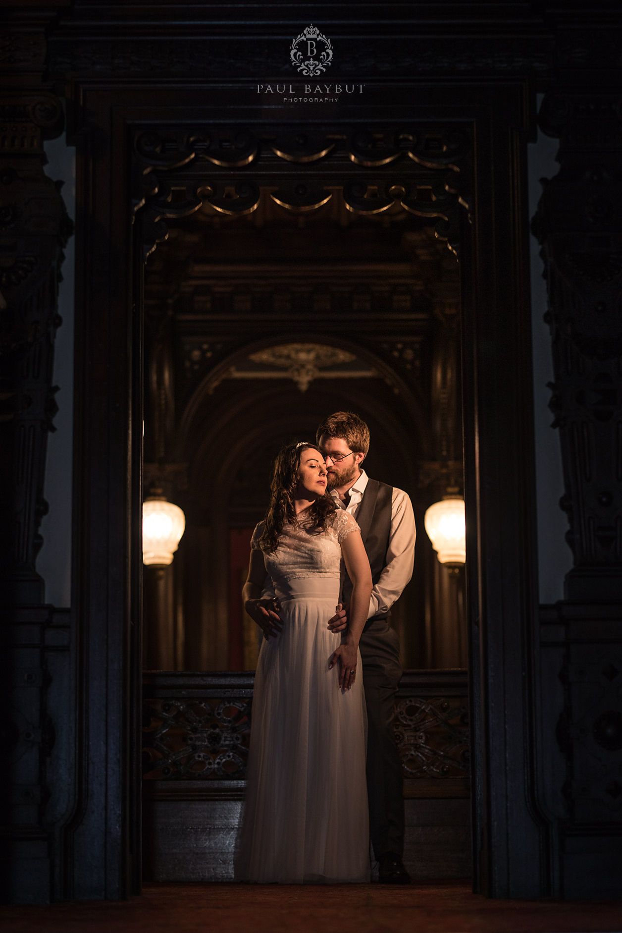 Romantic couple illuminated by warm sconces in ornate gothic doorway at elegant venue.