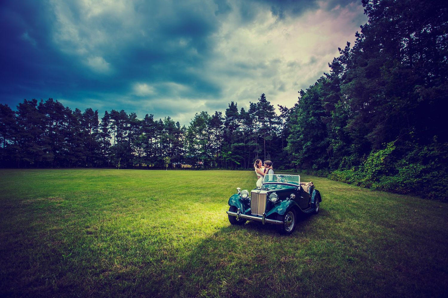 Vintage truck parked in a field against dramatic cloudy sky at sunset.