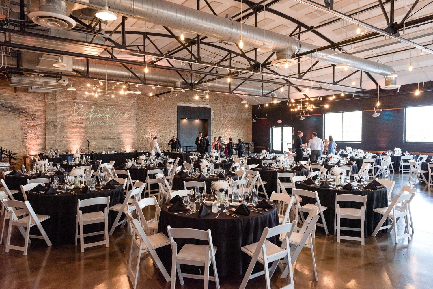 Industrial chic venue with exposed beams and white chairs set up for a wedding reception.