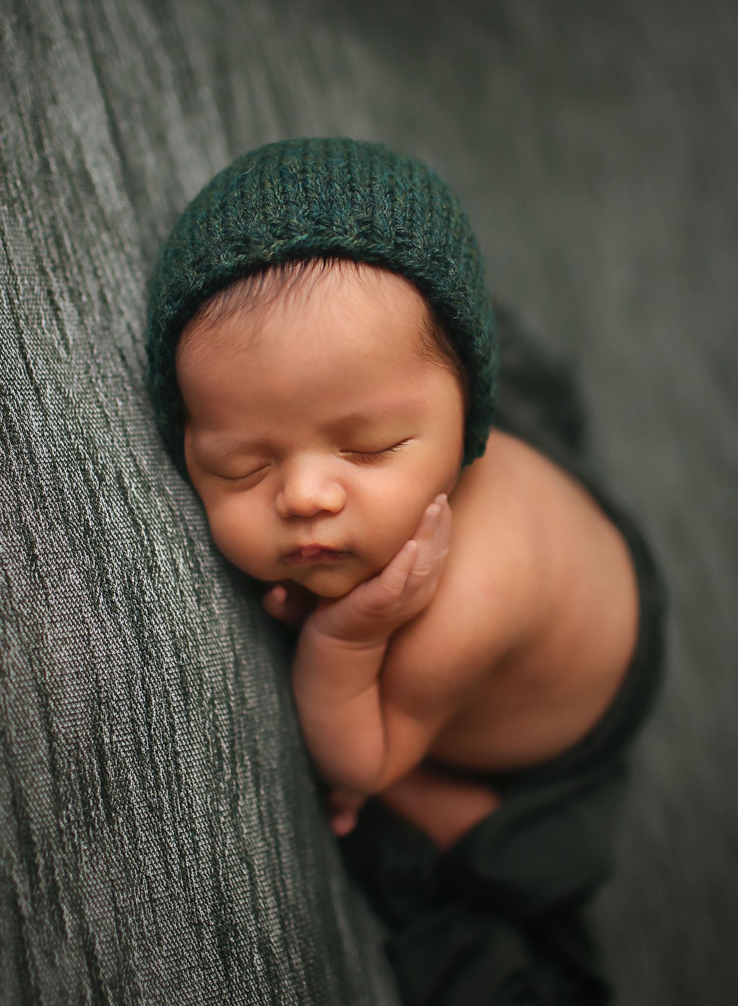 Perfect posed newborn boy with hand on. cheek laying on belly in Angleton, Tx photography studio