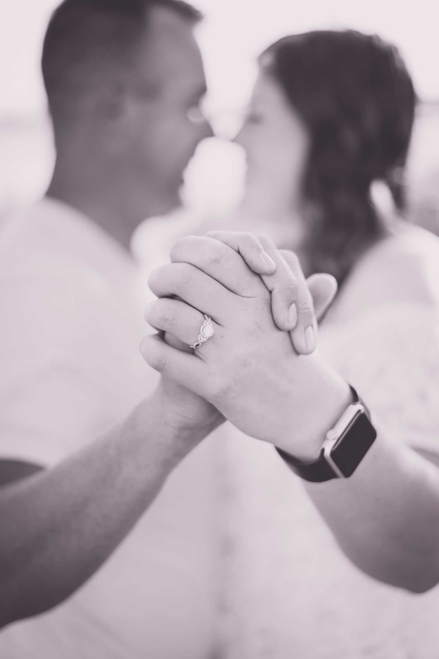 Close-up of joined hands with engagement ring and smart watch in soft focus black and white.
