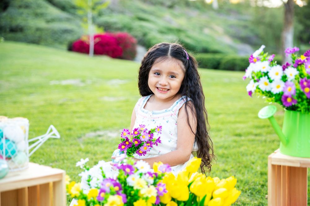 Orange County photographer captures Sweet young girl with long hair holds colorful flowers while sitting among blooms in a garden.