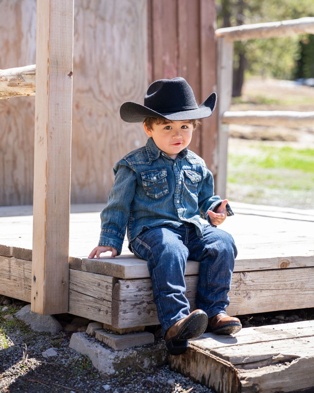 Orange County photographer captures  toddler in denim outfit and black cowboy hat sits on wooden steps at a ranch.