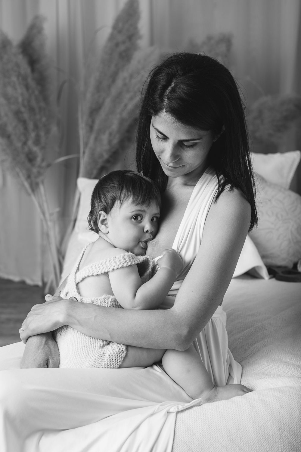 An intimate black and white portrait showing tender moments between parent and baby on white bedding.