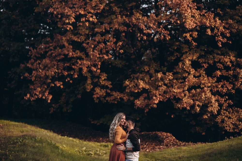 Couple embracing in autumn field with orange fall foliage.