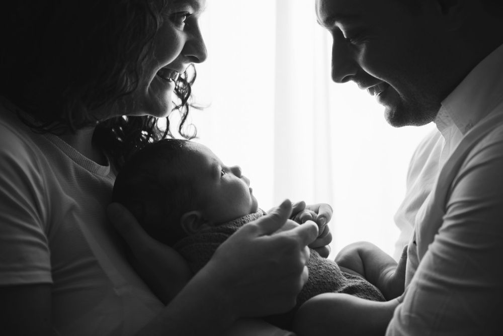 Intimate black and white portrait of family with newborn baby in soft window light.