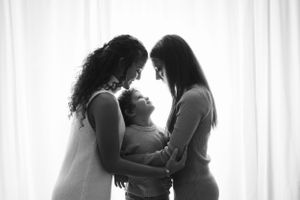 A tender black and white portrait of a family sharing an intimate moment together against a light background.