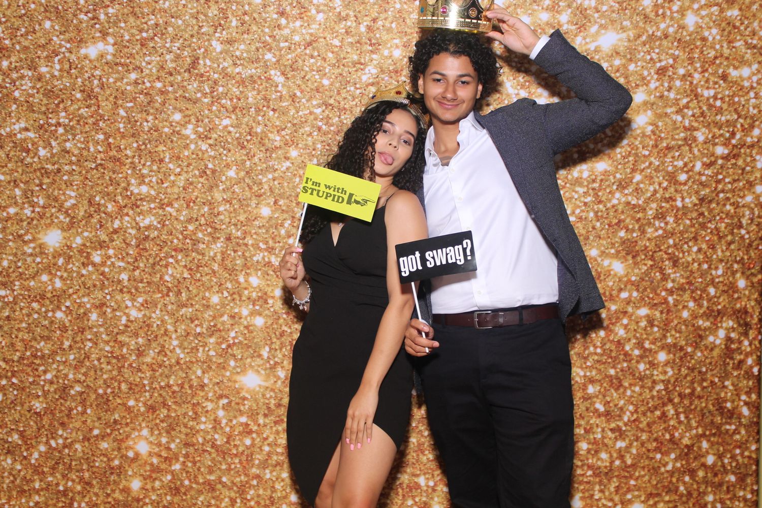 Party photo booth shot of couple with props against sparkly gold backdrop.