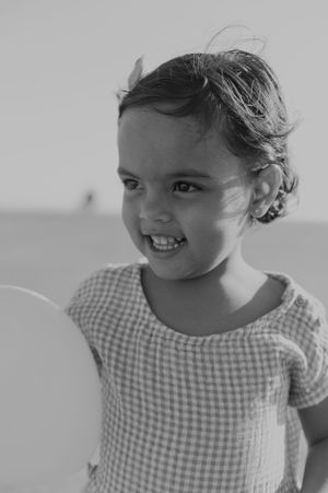 A black and white portrait of a young child wearing a gingham top and smiling brightly.