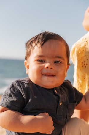 A cheerful toddler at the beach wearing a navy blue shirt on a sunny day.