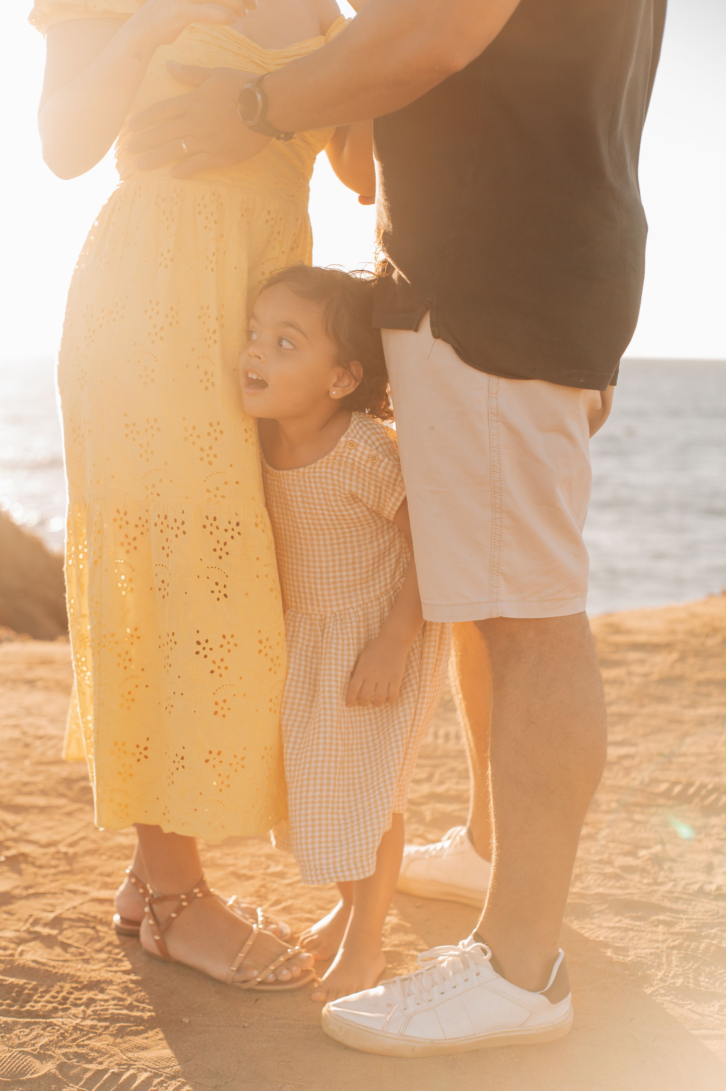 Child standing between adults at sunset wearing a checkered dress.