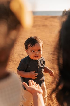 Young child in a black shirt smiles while standing on sandy ground at sunset.