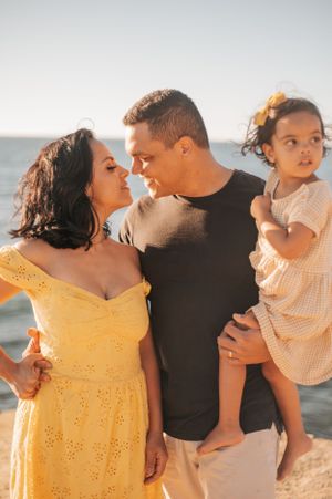 A family shares a loving moment on the beach, with the woman wearing a yellow sundress.