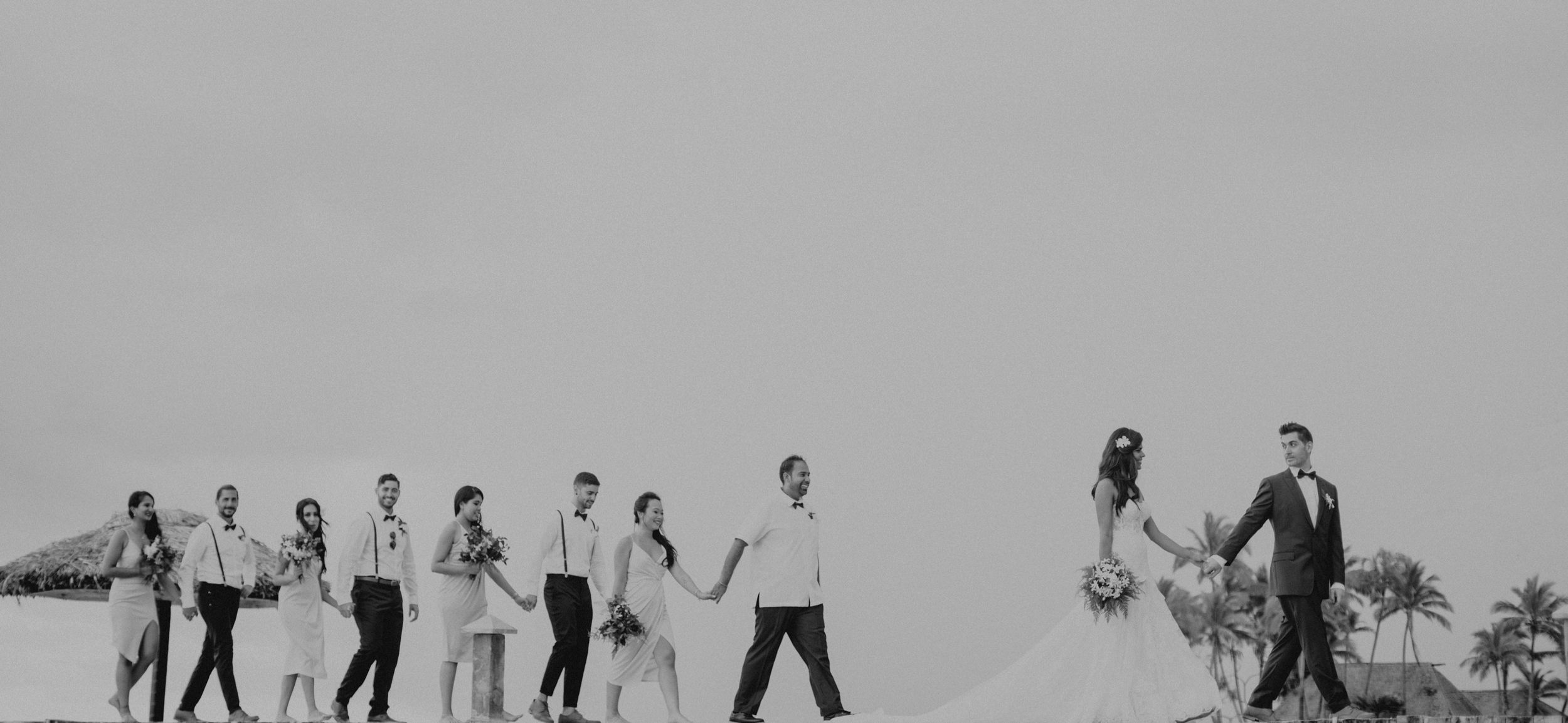 Artistic black and white photo of wedding party walking along horizon.