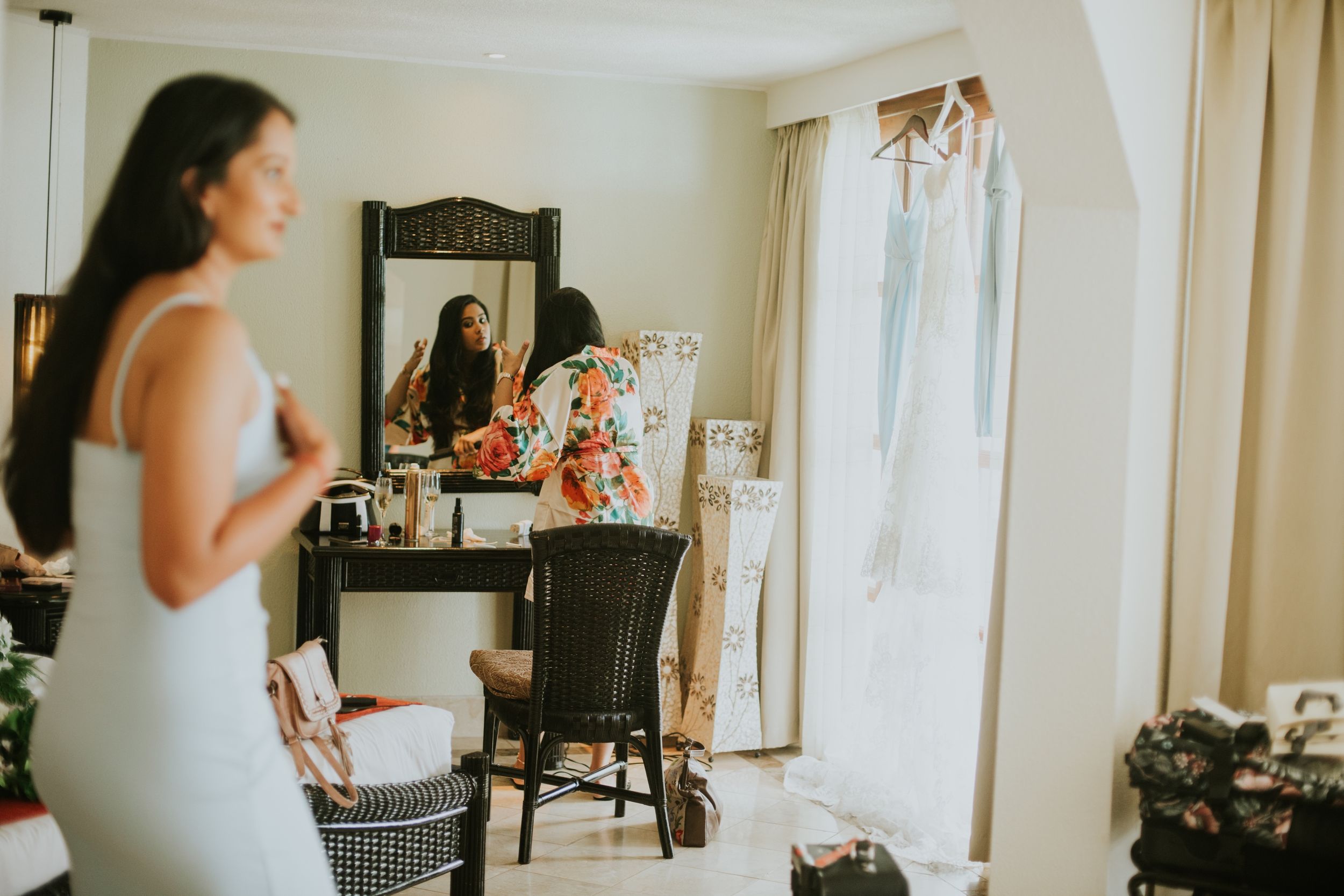 Bride getting ready in front of a vanity mirror in a sunlit room with white decor.