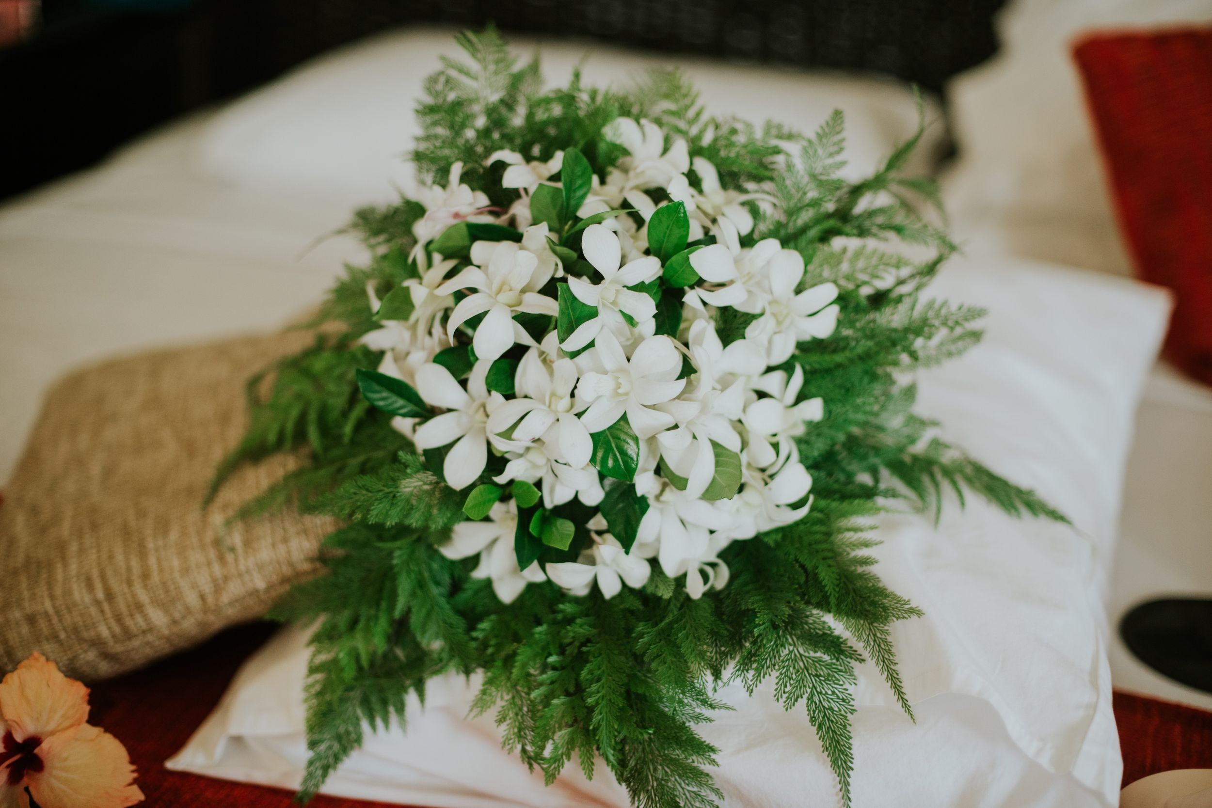 White floral bouquet with ferns arranged on light fabric.