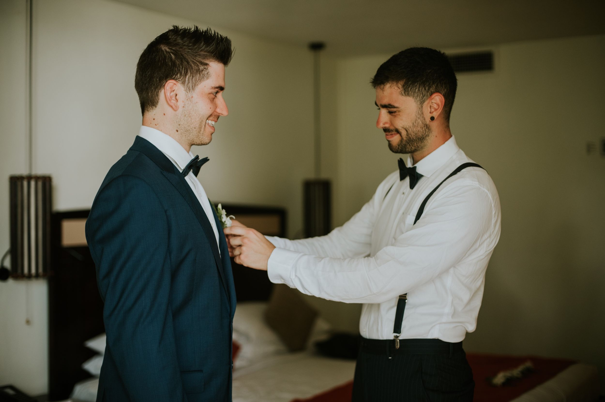 Groomsmen helping with formal attire preparations before wedding ceremony.