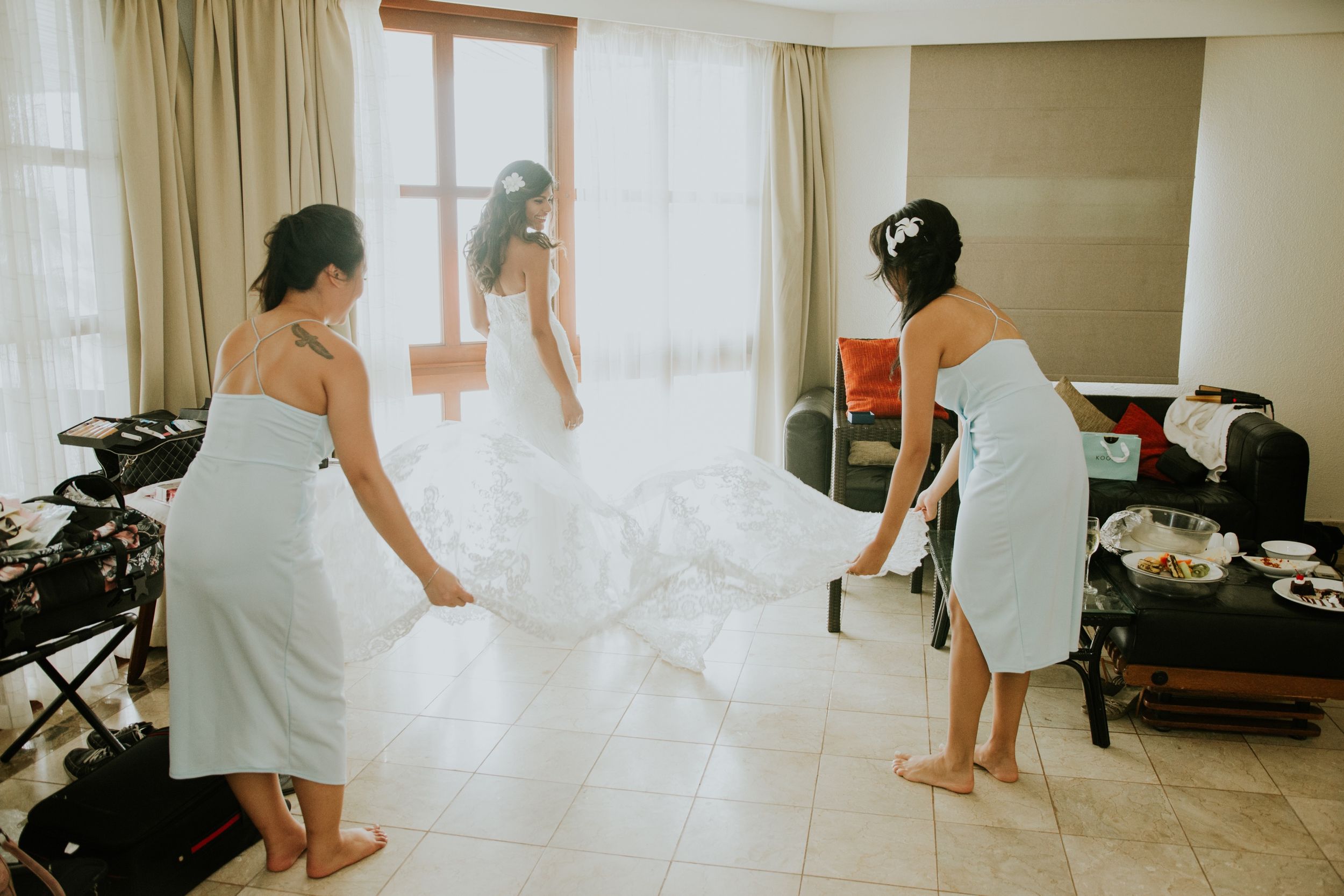 Women in white robes jumping playfully on a bed during wedding preparations.