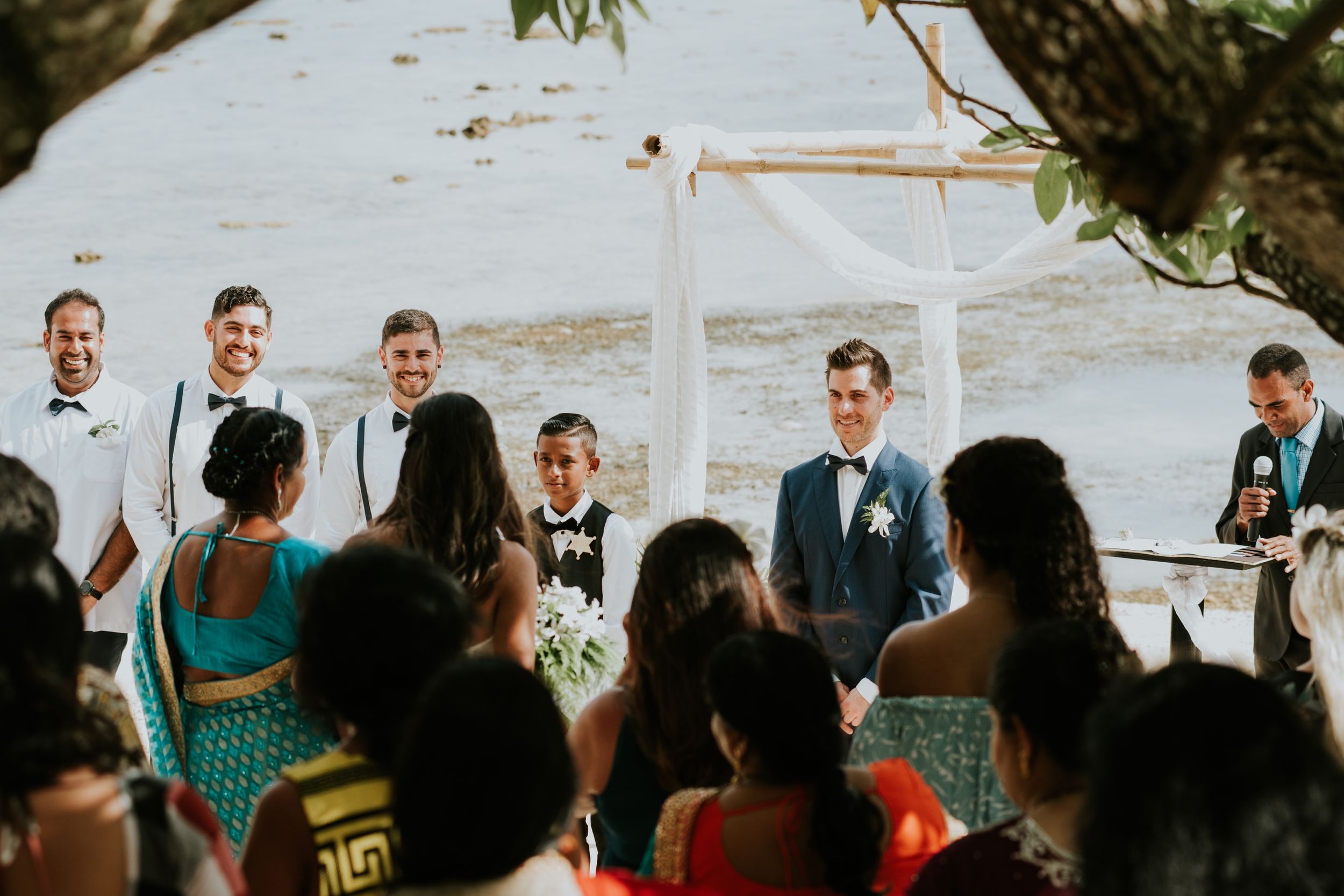 Outdoor beach wedding ceremony with guests seated facing an ocean backdrop.