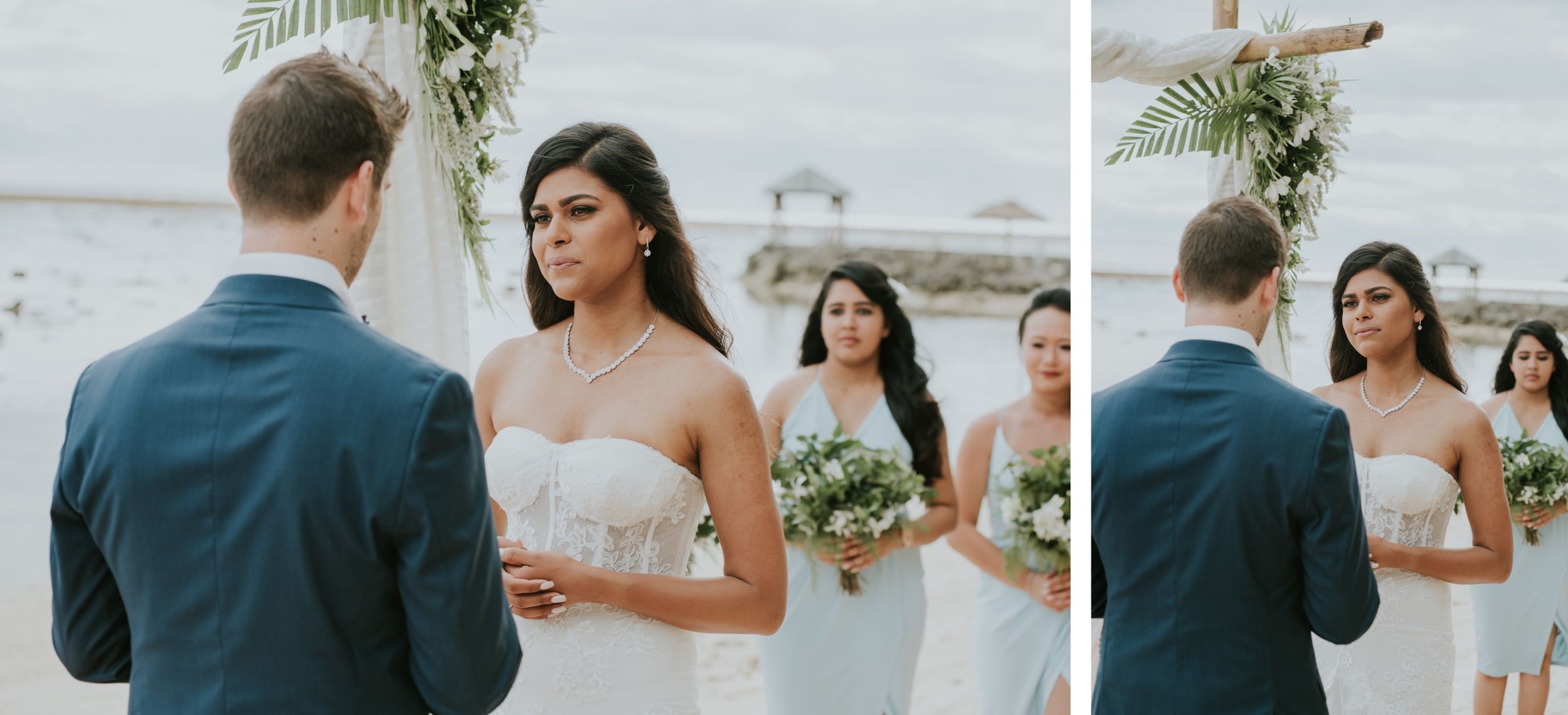 A couple shares their wedding vows under a decorated arch with palm fronds on a sunny beach.