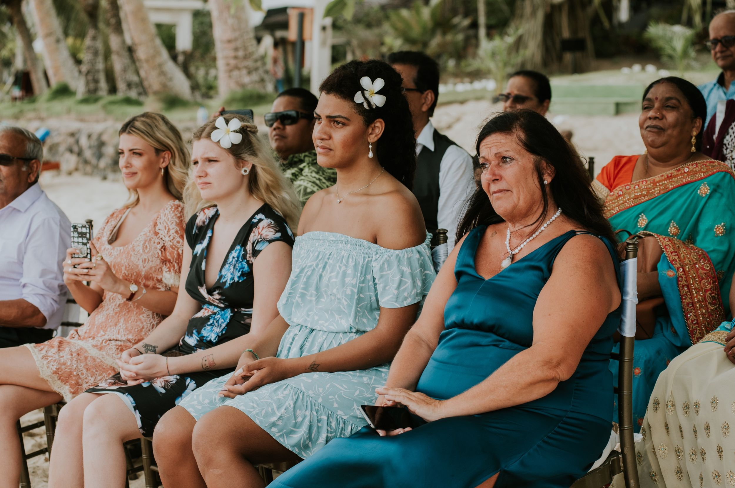 Wedding guests seated in casual attire watch the ceremony outdoors.